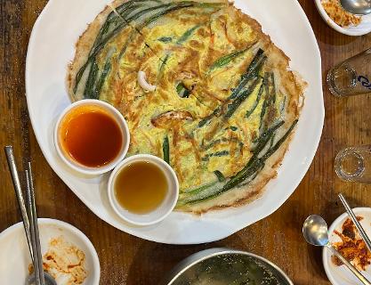 하얀 접시에 담긴 동래할매파전과 소스, 반찬, 잔이 놓인 테이블 장면