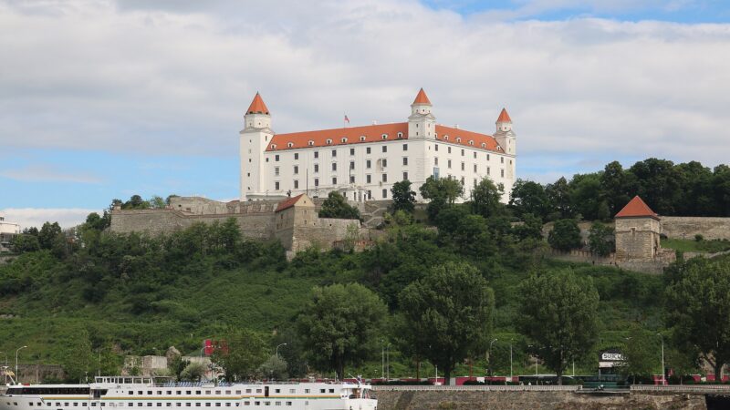 언덕 위 흰 성벽과 붉은 지붕 네 개의 탑이 보이는 브라티슬라바 성과 다뉴브강 전경