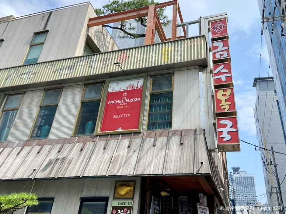 부산 해운대 금수복국 해운대본점 외관과 미쉐린 배너, 붉은 세로 간판이 보이는 거리 풍경