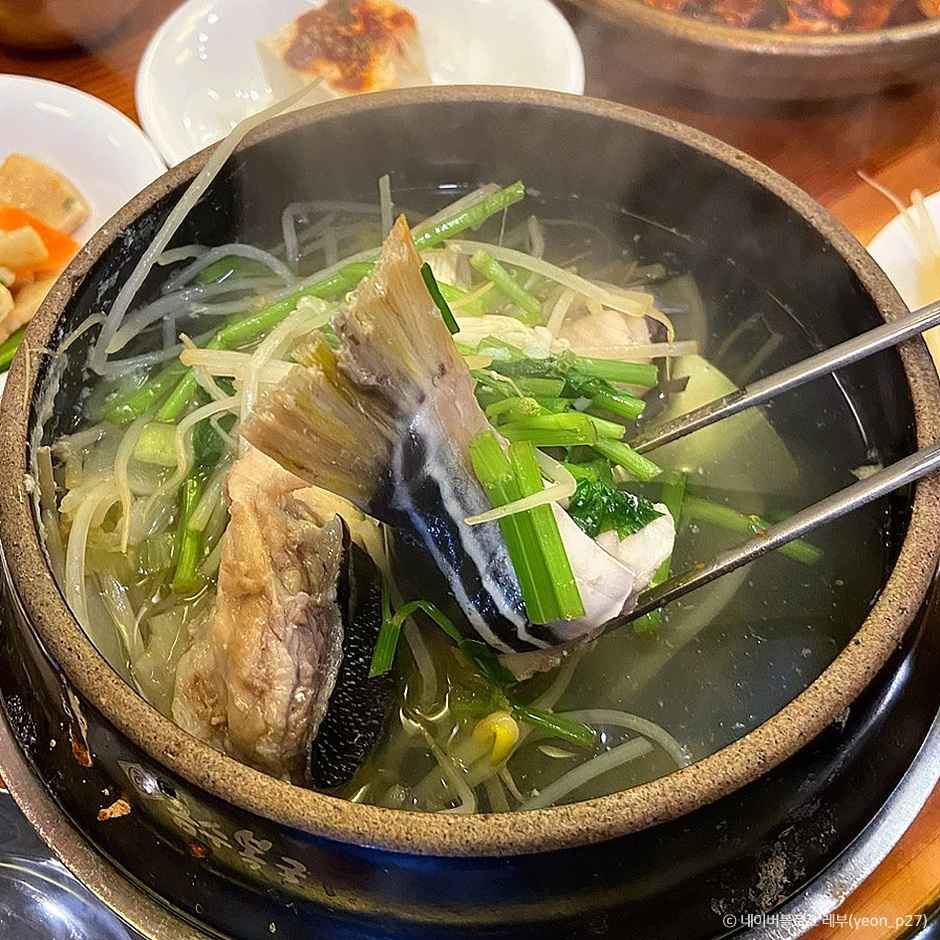 부산 금수복국 해운대본점 복국 뚝배기에서 복어 살과 콩나물, 미나리가 보이는 클로즈업