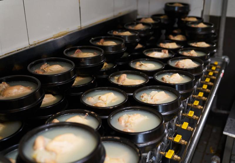 고려삼계탕 주방에서 검은 뚝배기 여러 개에 삼계탕을 올려두고 준비하는 장면