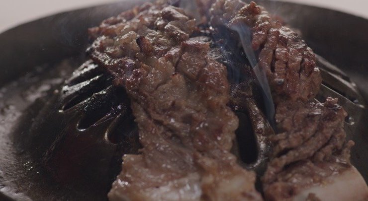 집게로 들어 올린 해운대암소갈비집의 구워진 소갈비 한 점과 뜨거운 불판
