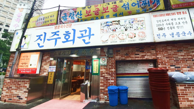 붉은 벽돌 외관과 큰 진주회관 간판, 비에 젖은 길바닥이 함께 보이는 시청 진주회관 정면