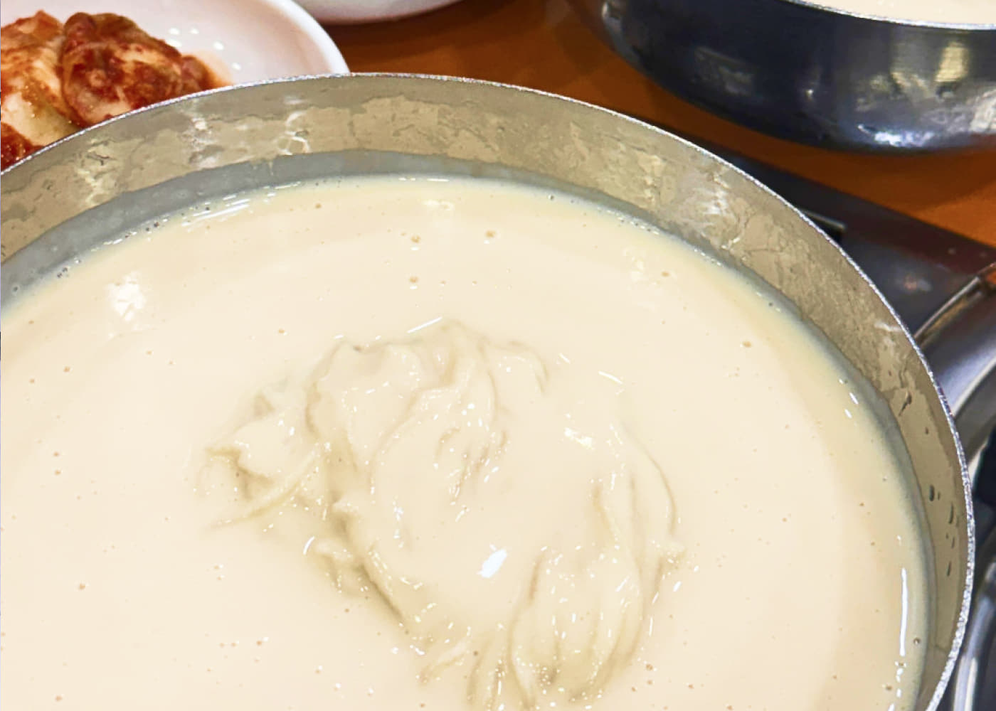 걸쭉한 콩물이 담긴 큰 금속 그릇 위로 면이 올라온 진주회관 콩국수 한 그릇