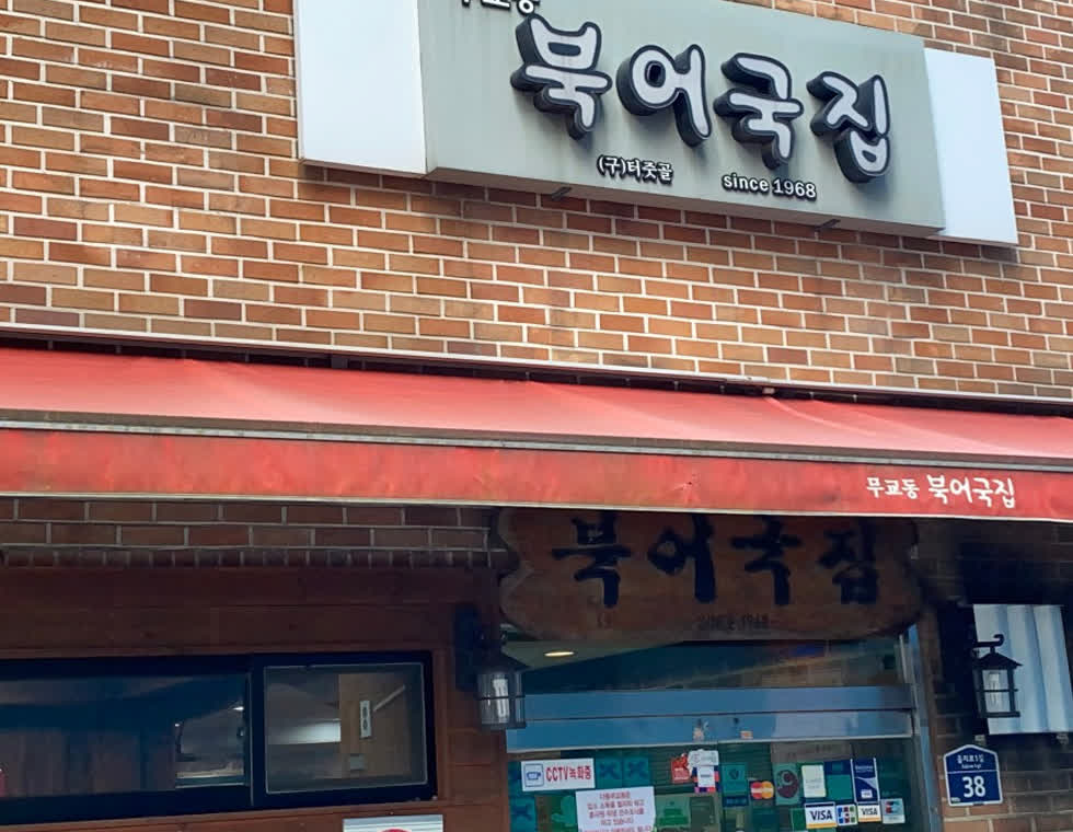 큰 북어국집 간판과 붉은 차양, 입구 스티커가 가까이 보이는 무교동북어국집 입면