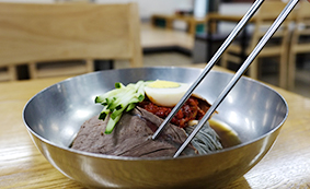 서울 오장동흥남집 본점 회냉면 한 그릇에 고기와 채소 고명, 젓가락이 보이는 모습