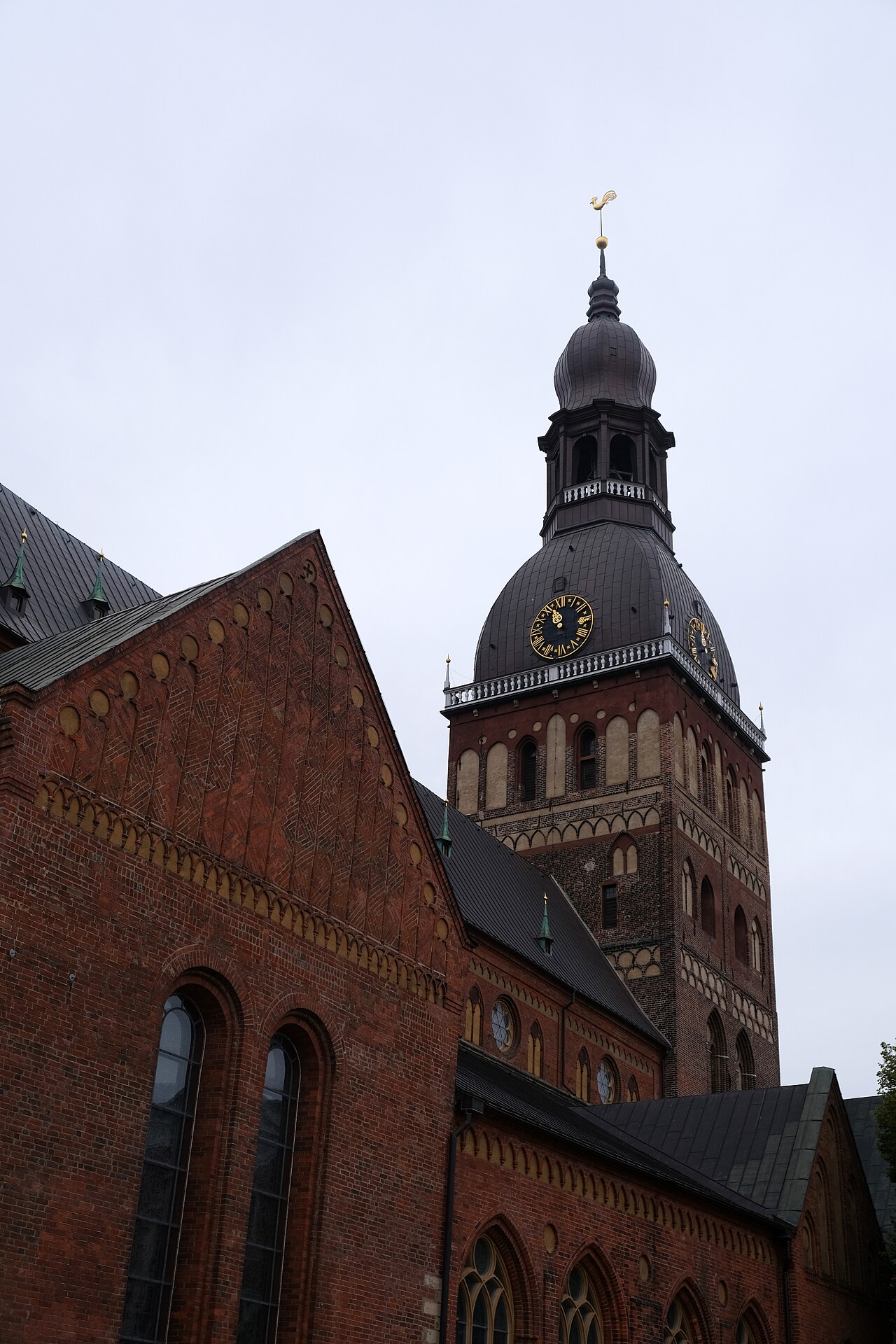 붉은 벽돌 외벽과 시계가 달린 돔형 탑이 보이는 리가 대성당 외관