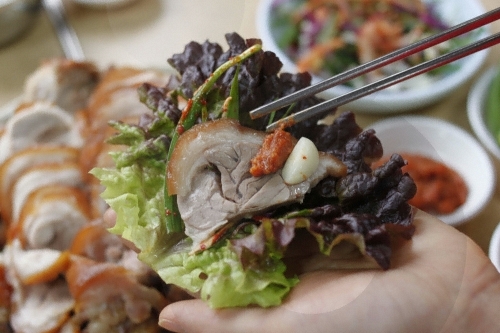 상추에 족발과 양념을 올려 쌈으로 먹는 모습과 뒤쪽의 족발 접시