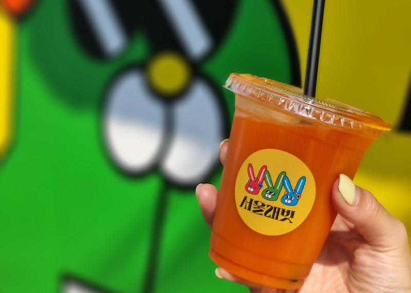 서울 래빗 시그니처 당근 음료 한 잔을 토끼 벽화 앞에서 가까이 찍은 모습