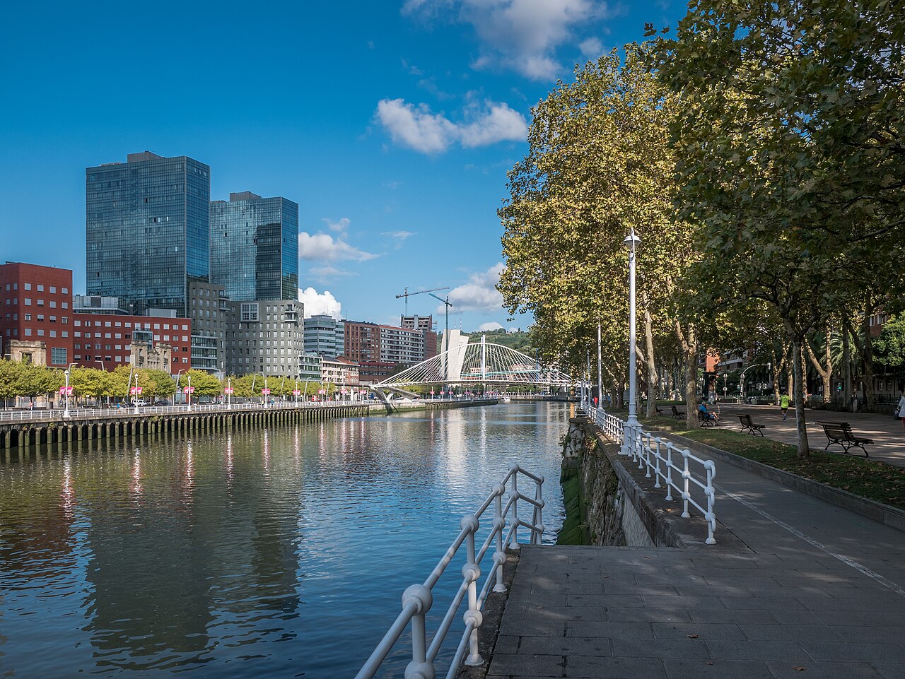 네르비온강 위로 흰 아치형 케이블 구조가 보이는 빌바오 주비주리 다리와 강변 산책로