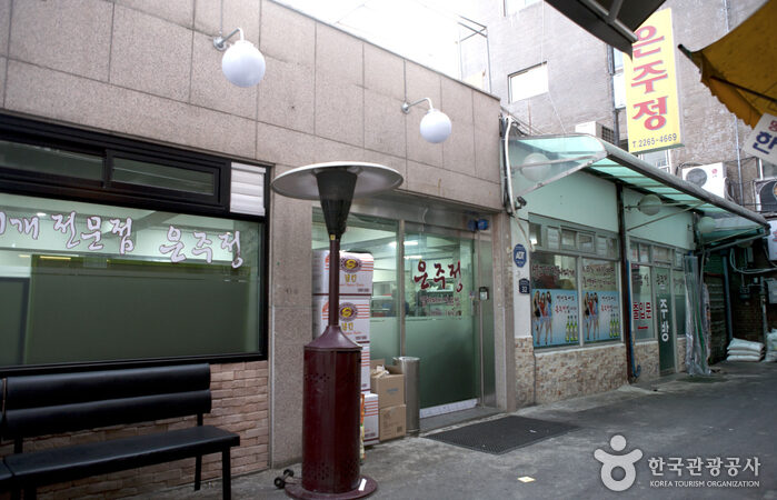 은주정 외관과 벤치, 붉은 난로가 보이는 주교동 골목 입구 풍경