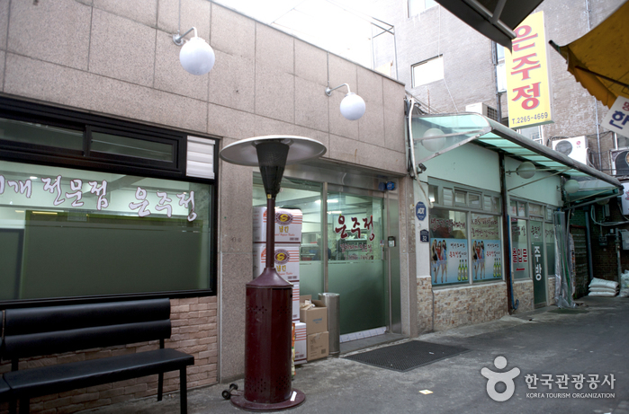은주정 외관과 벤치, 붉은 난로가 보이는 주교동 골목 입구 풍경