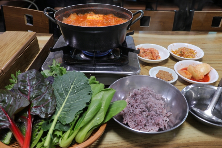 붉게 끓는 김치찌개 냄비와 쌈채소, 밥, 반찬이 함께 놓인 은주정 한 상
