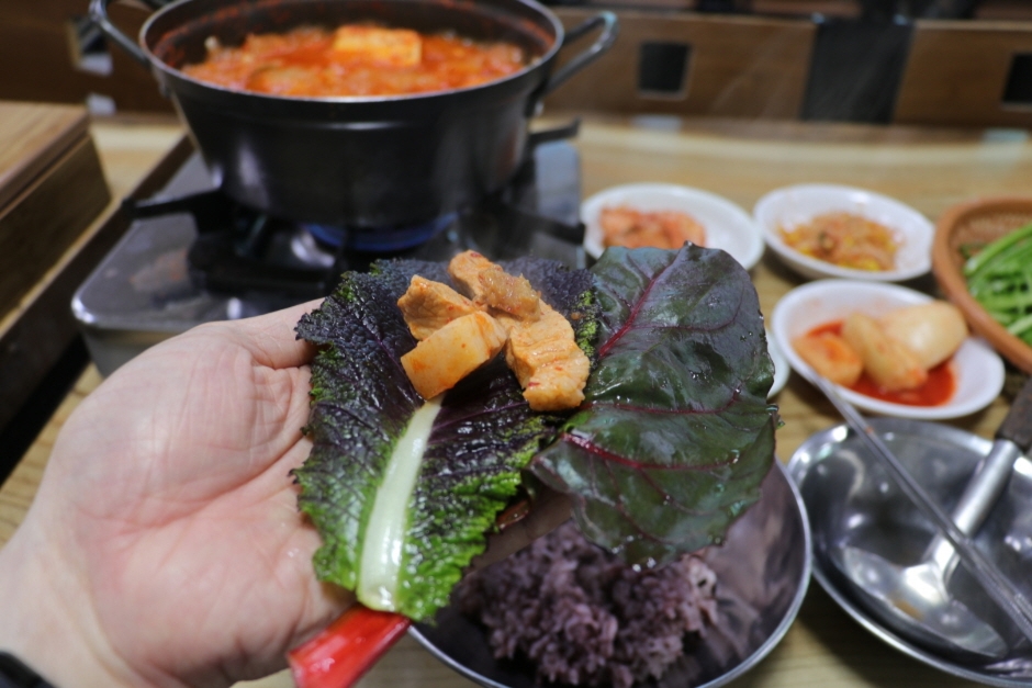 은주정 김치찌개와 삼겹살을 쌈채소에 싸 들고 있는 손과 식탁 장면