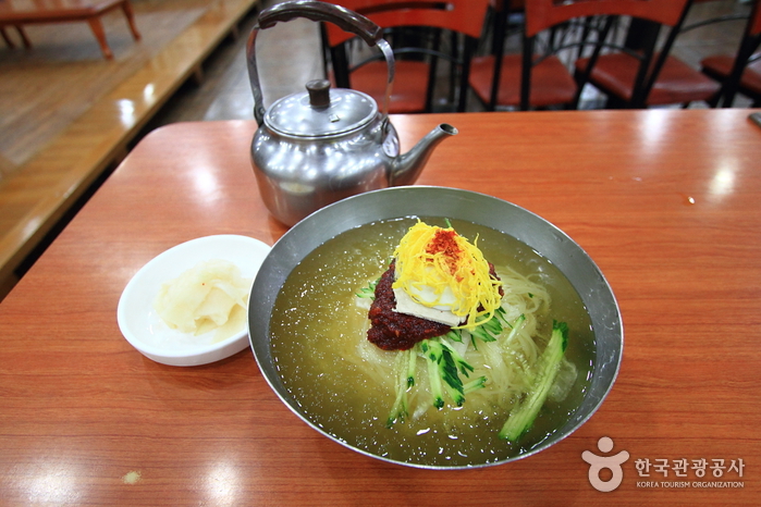 가야할매밀면의 밀면 한 그릇과 오이, 계란, 양념이 올라간 금속 그릇 상차림
