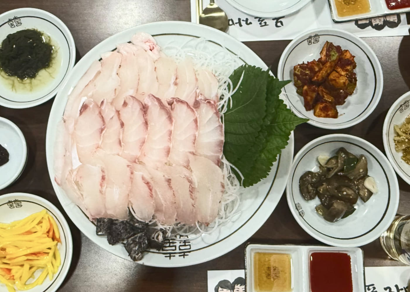목포자매집의 흰살생선 회 접시와 깻잎, 여러 반찬, 소스가 함께 놓인 상차림