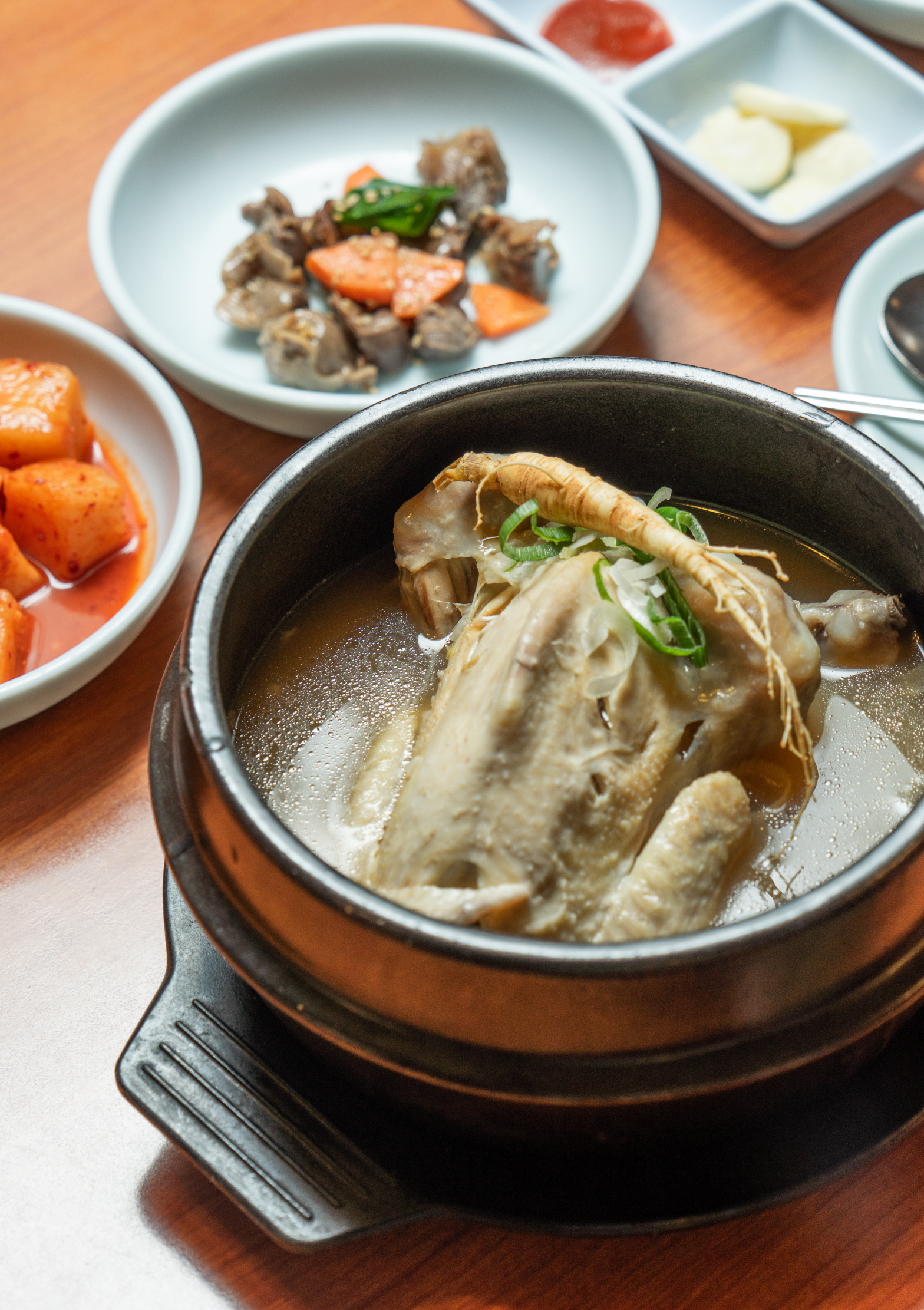 종로삼계탕의 검은 뚝배기 삼계탕과 깍두기, 마늘, 반찬이 함께 놓인 상차림