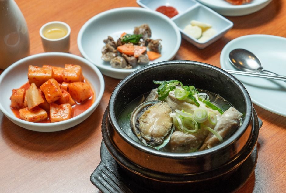 종로삼계탕의 전복이 올라간 뚝배기와 깍두기, 반찬이 보이는 상차림 클로즈업